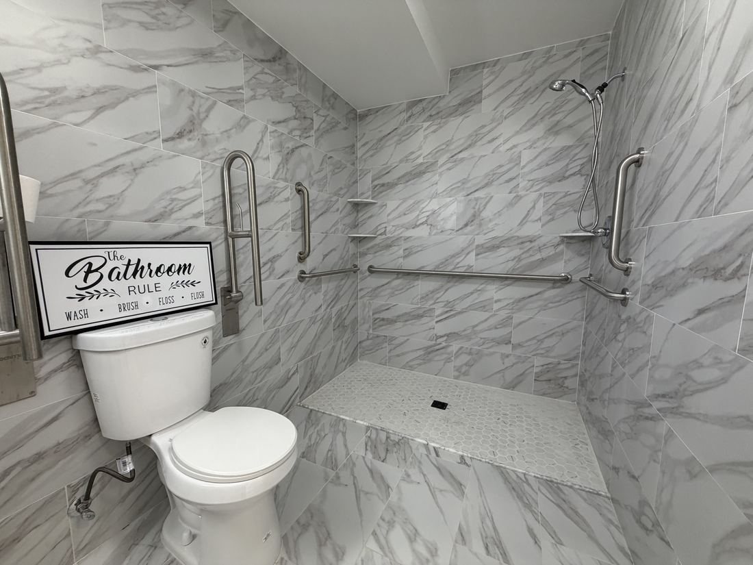 A resident bathroom with a toilet and a walk-in shower with grab bars.