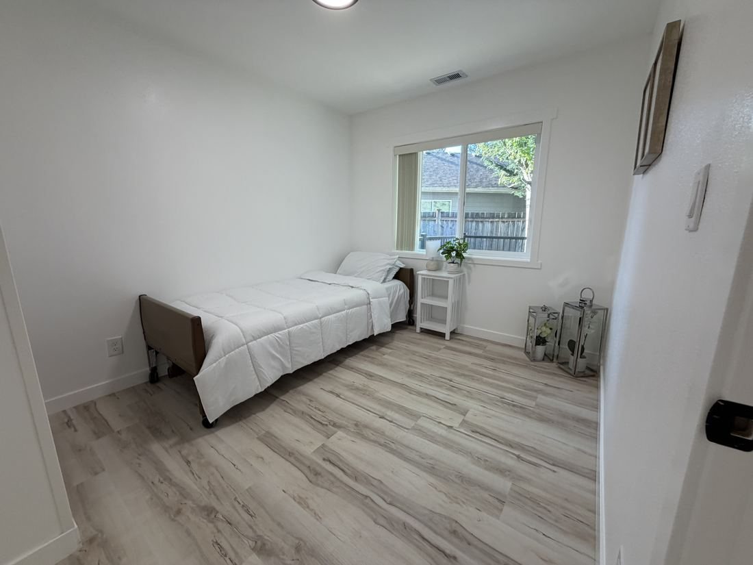 A resident bedroom with a bed, a window and a wood-look floor.